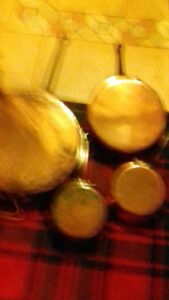 Blurry image of several copper pans, including casseroles and sauté pans, hanging on a wall with a tiled background.